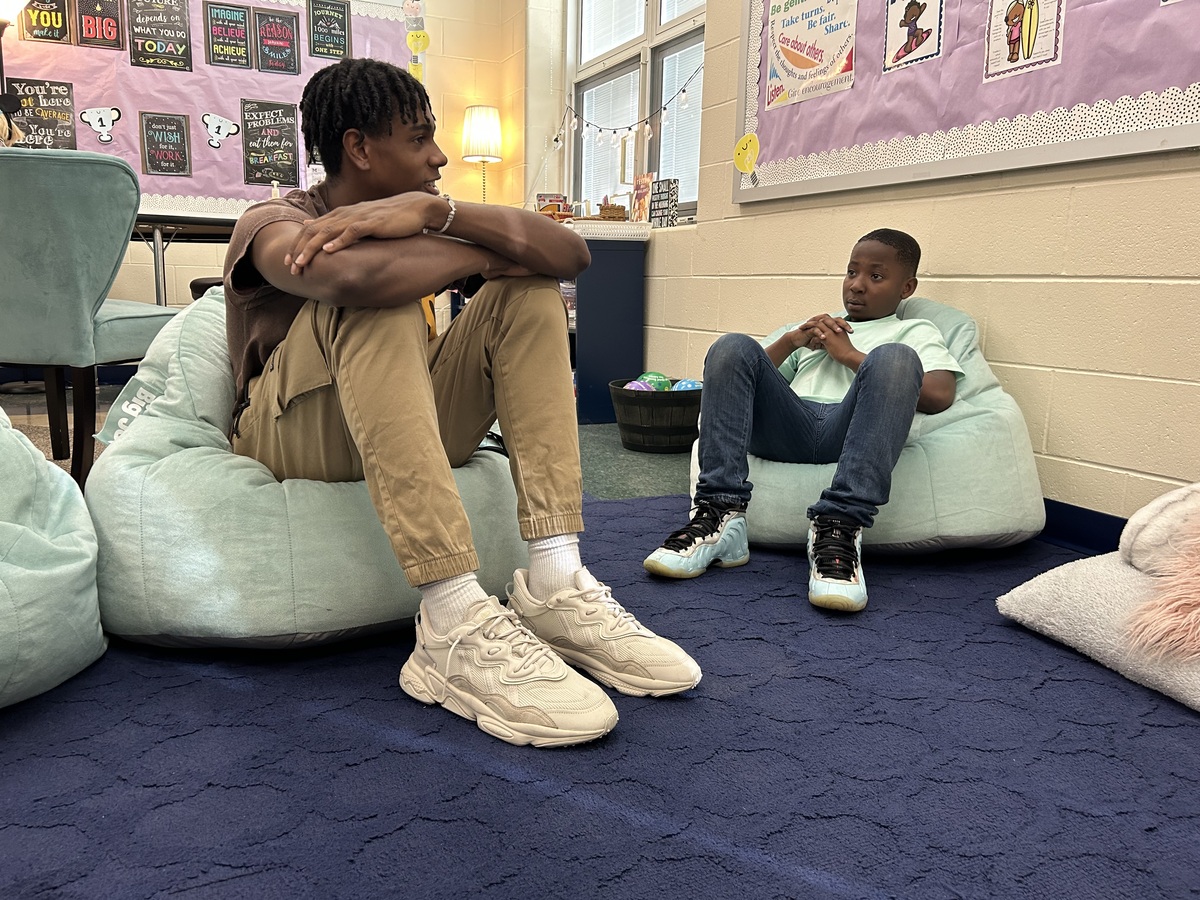 Older student and younger student sit on bean bags together.