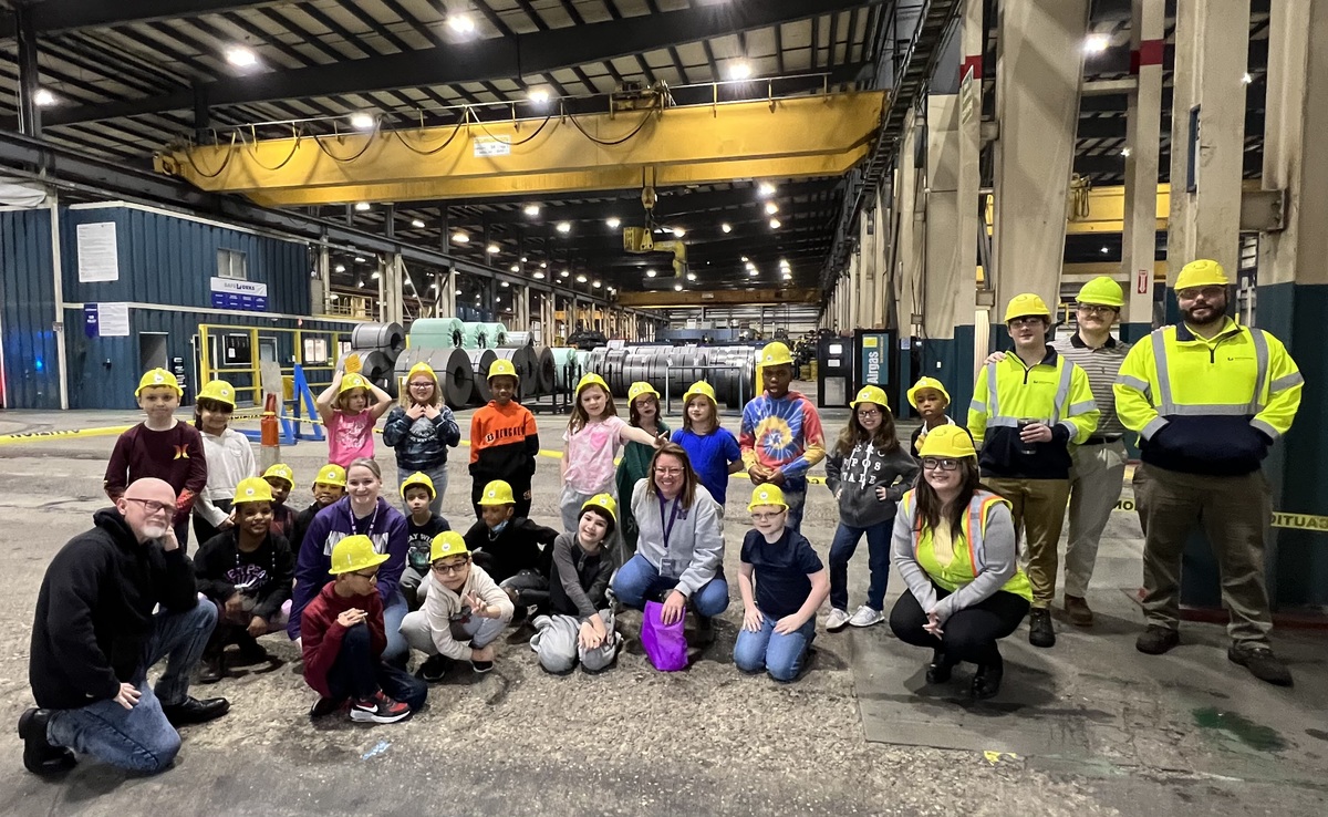 Students pose for photo wearing hardhats inside Worthington Industries