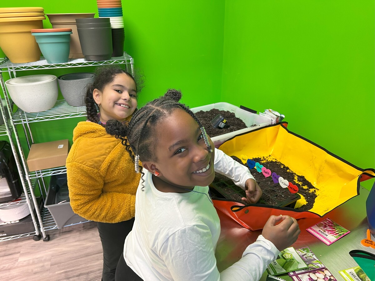 Two young girls smile for the camera while planting seeds in new food lab.