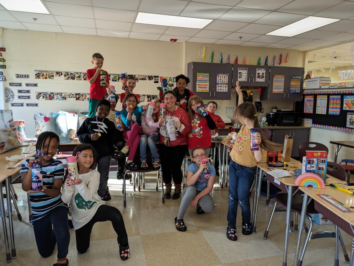 Group photo of third graders and their teacher holding up Christmas gifts donated to them.