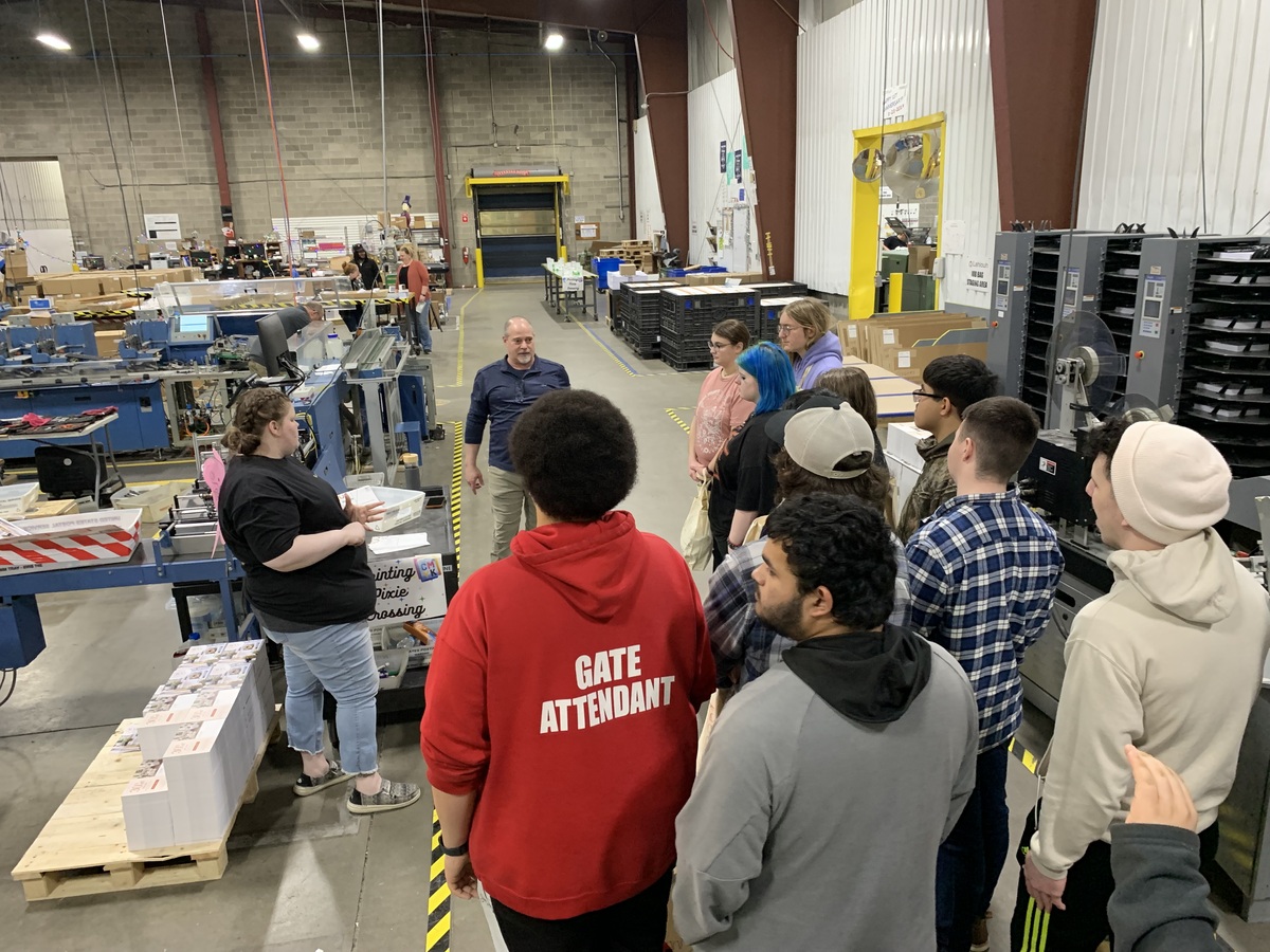 Group of students listen to demonstration inside warehouse