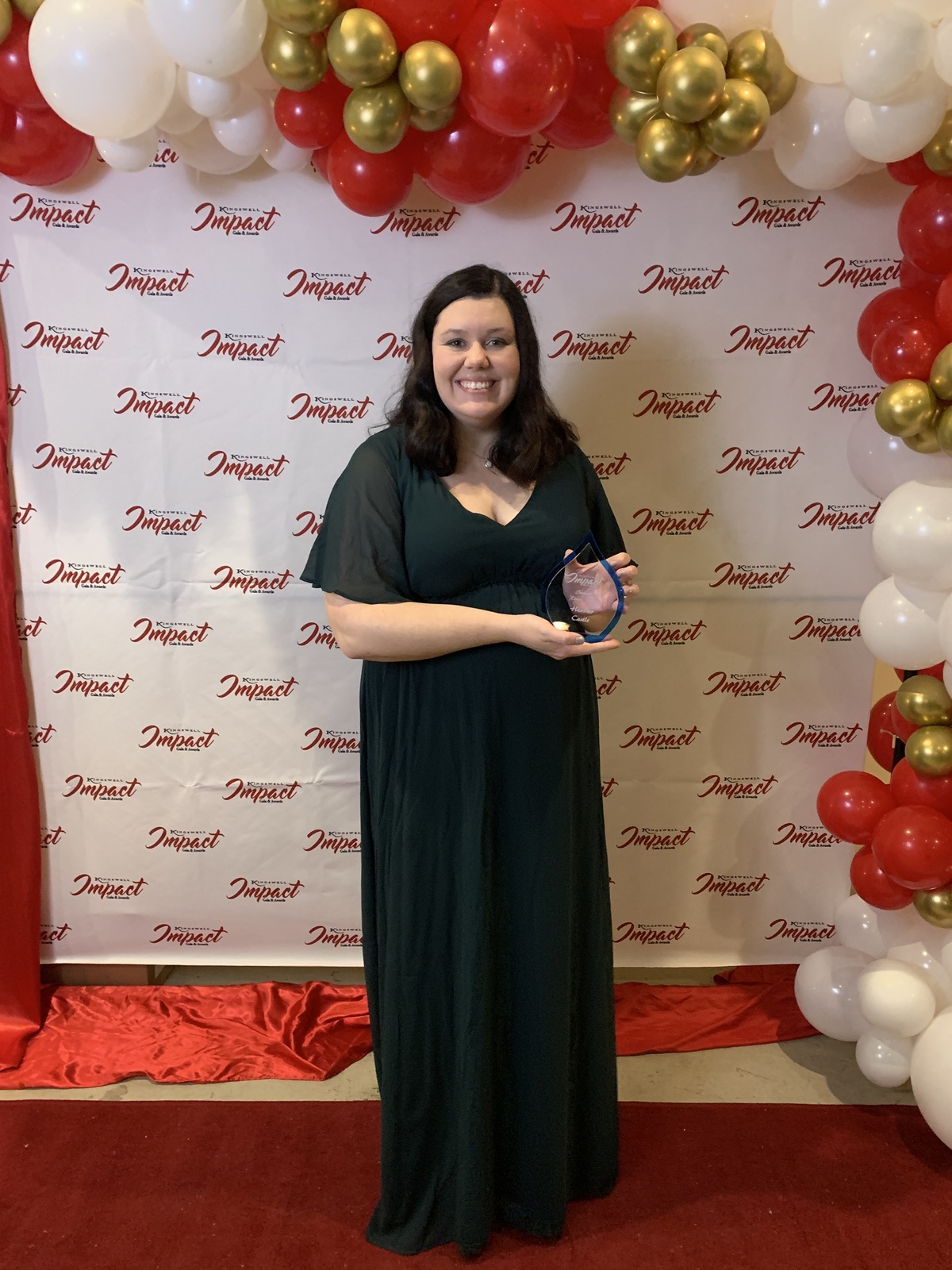 Woman wearing dress, holds up award against photo backdrop
