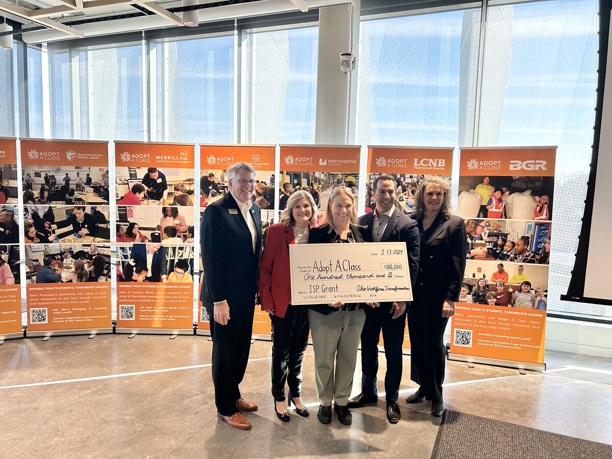 Five people hold up large $100,000 grant check in front of banners for Adopt A Class