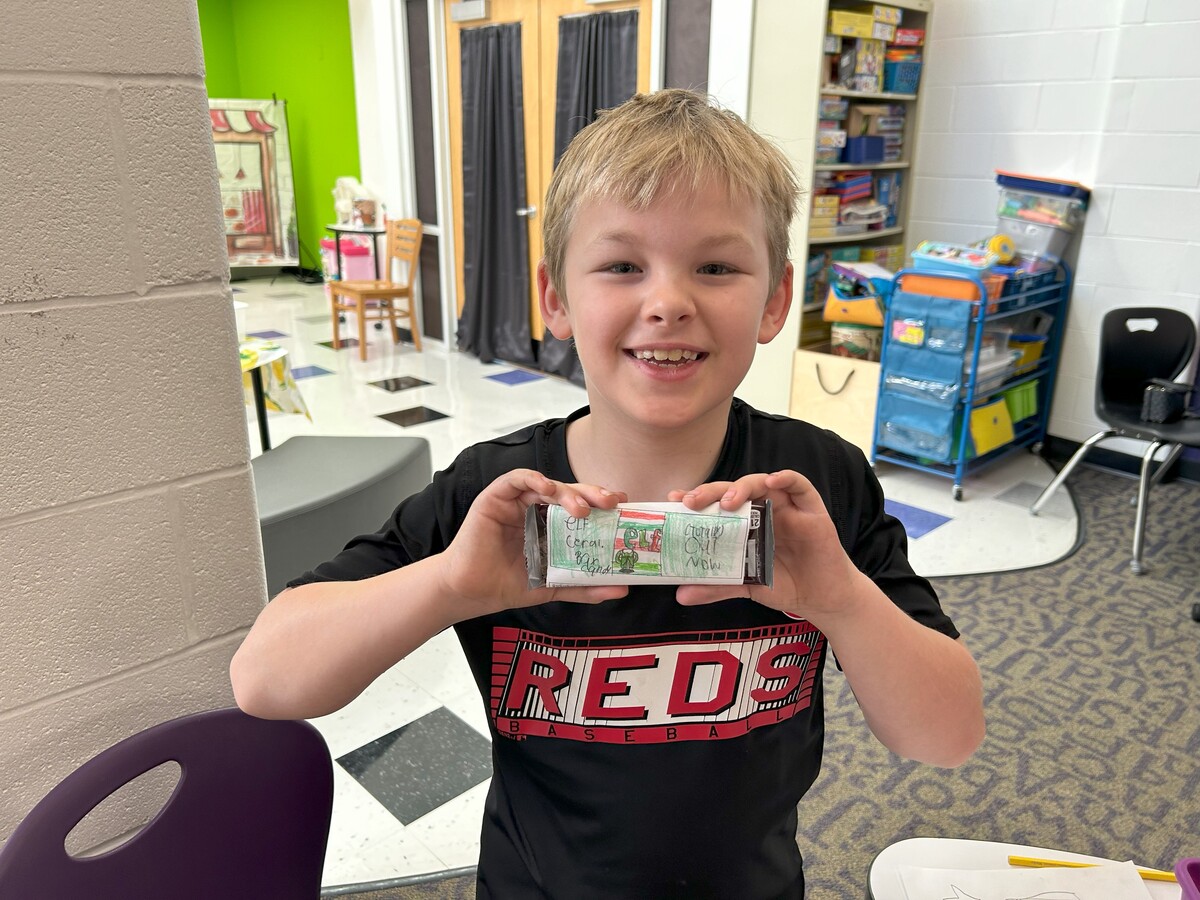 Student smiles and holds up candy bar wrapper he designed